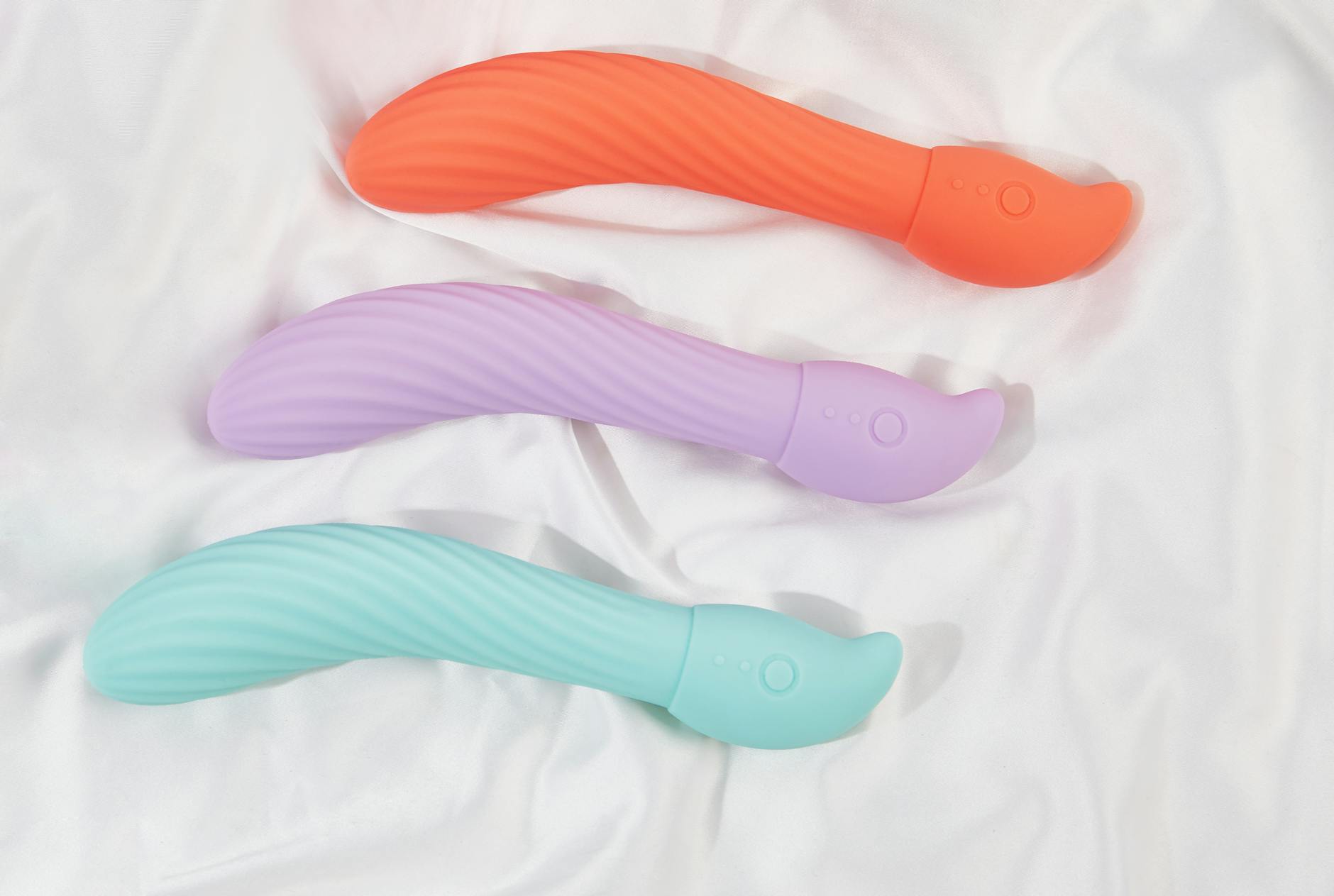 A teal clitoral vibrator on smooth white silk fabric, representing intimacy and pleasure