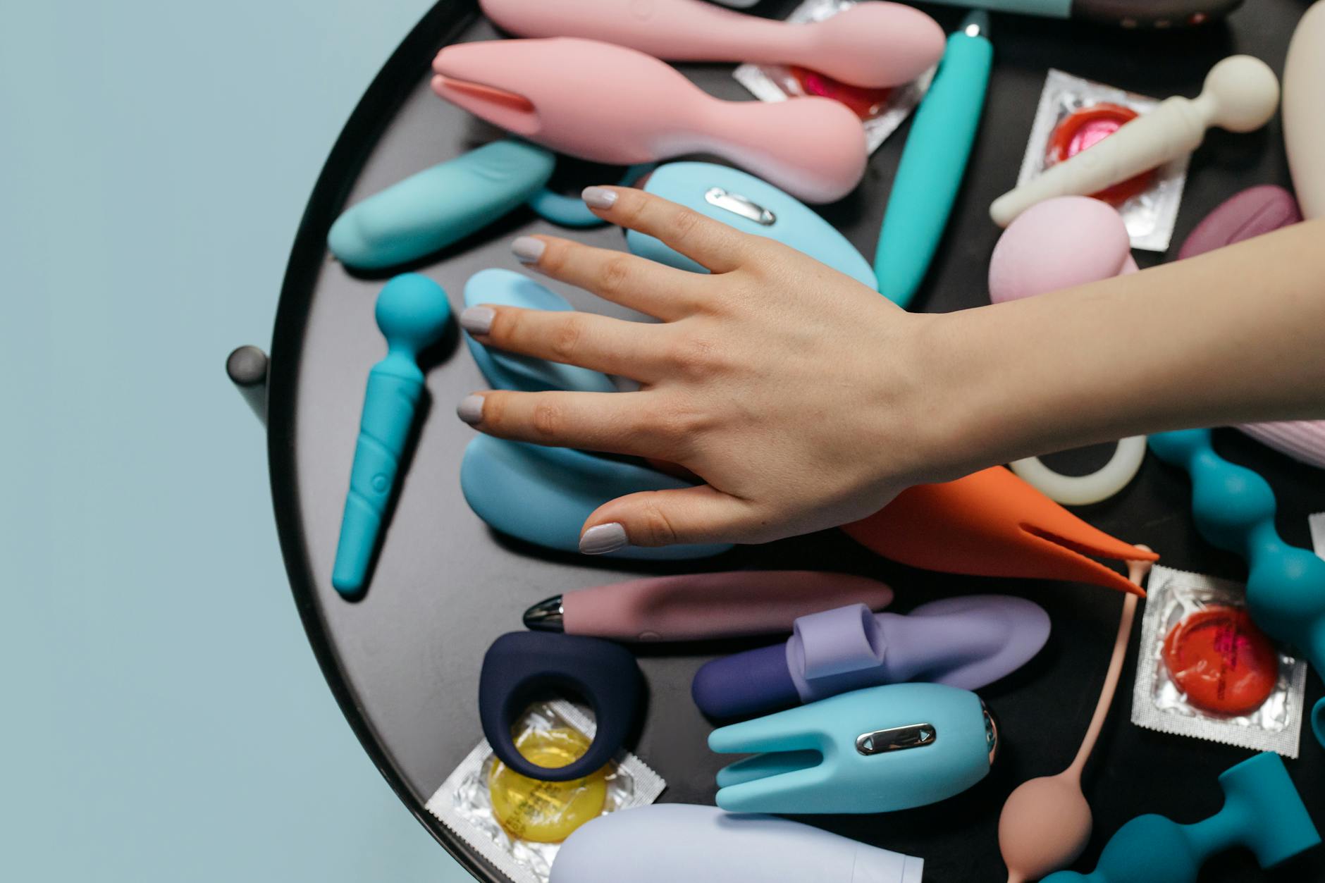 Close-up of hands exploring a variety of colorful adult toys together on a table